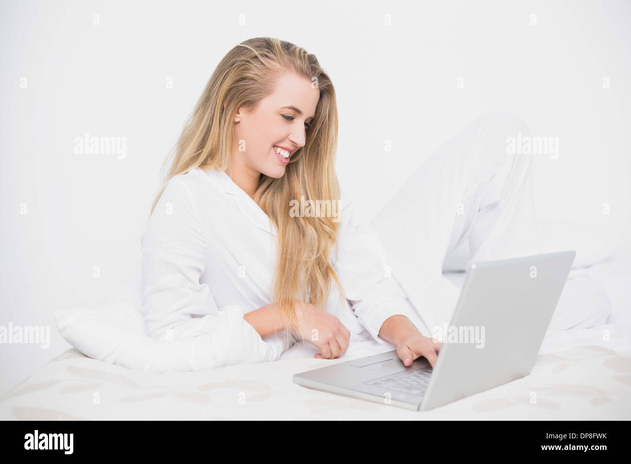 Sorridente piuttosto modello usando il suo computer portatile giacente sul letto confortevole Foto Stock