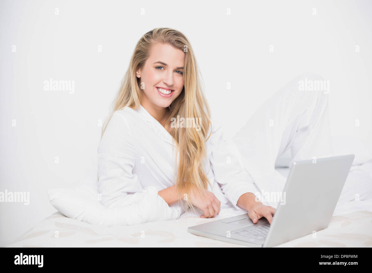 Allegro grazioso modello usando il suo computer portatile giacente sul letto confortevole Foto Stock