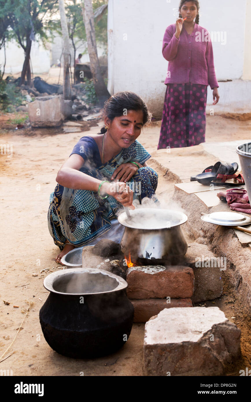 Donna indiana la cottura del riso su un fuoco aperto fuori la sua casa in un borgo rurale. Andhra Pradesh, India Foto Stock