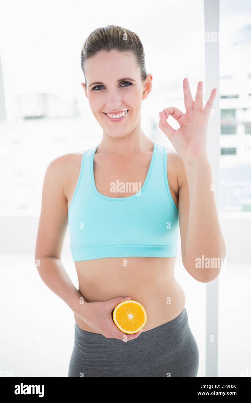 Modello sorridente in azienda di abbigliamento sportivo di fettine di arancia sul suo ventre Foto Stock