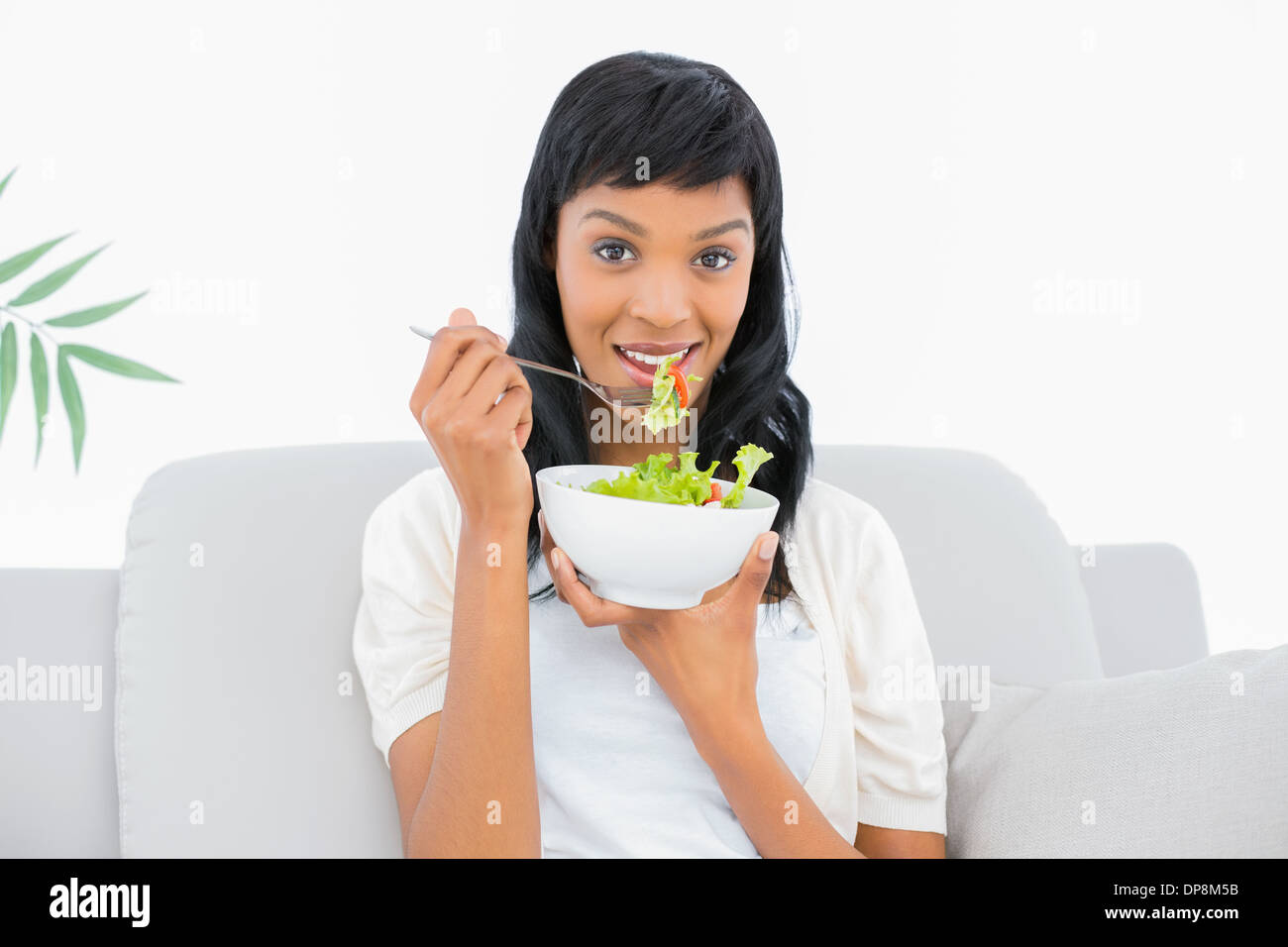 Affascinante dai capelli neri donna in vestiti di bianco mangiare insalata Foto Stock