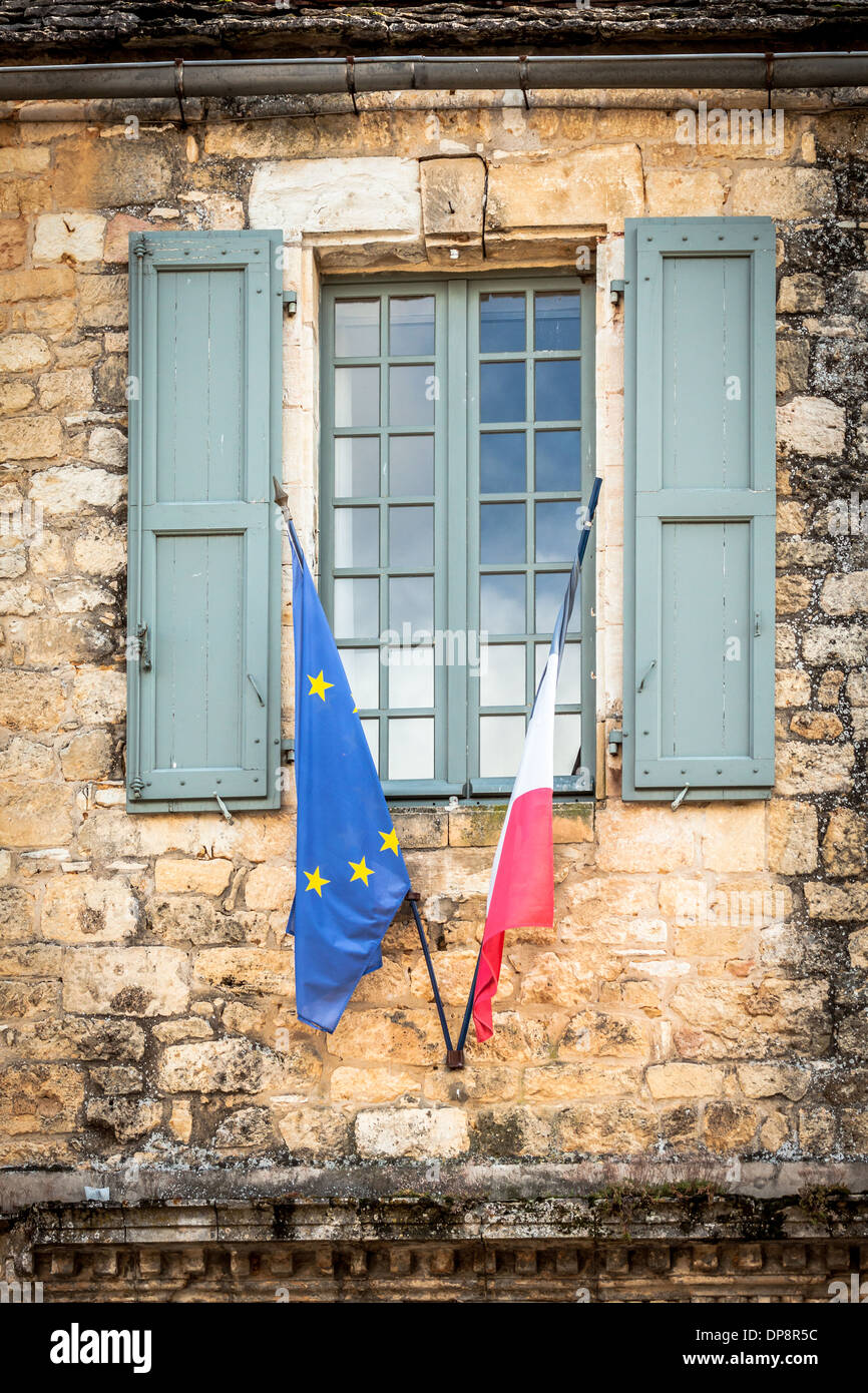 Domme, Dordogne, la Francia, l'Europa. Ue & bandiere francese di fronte a una vecchia finestra con persiane in legno. Foto Stock
