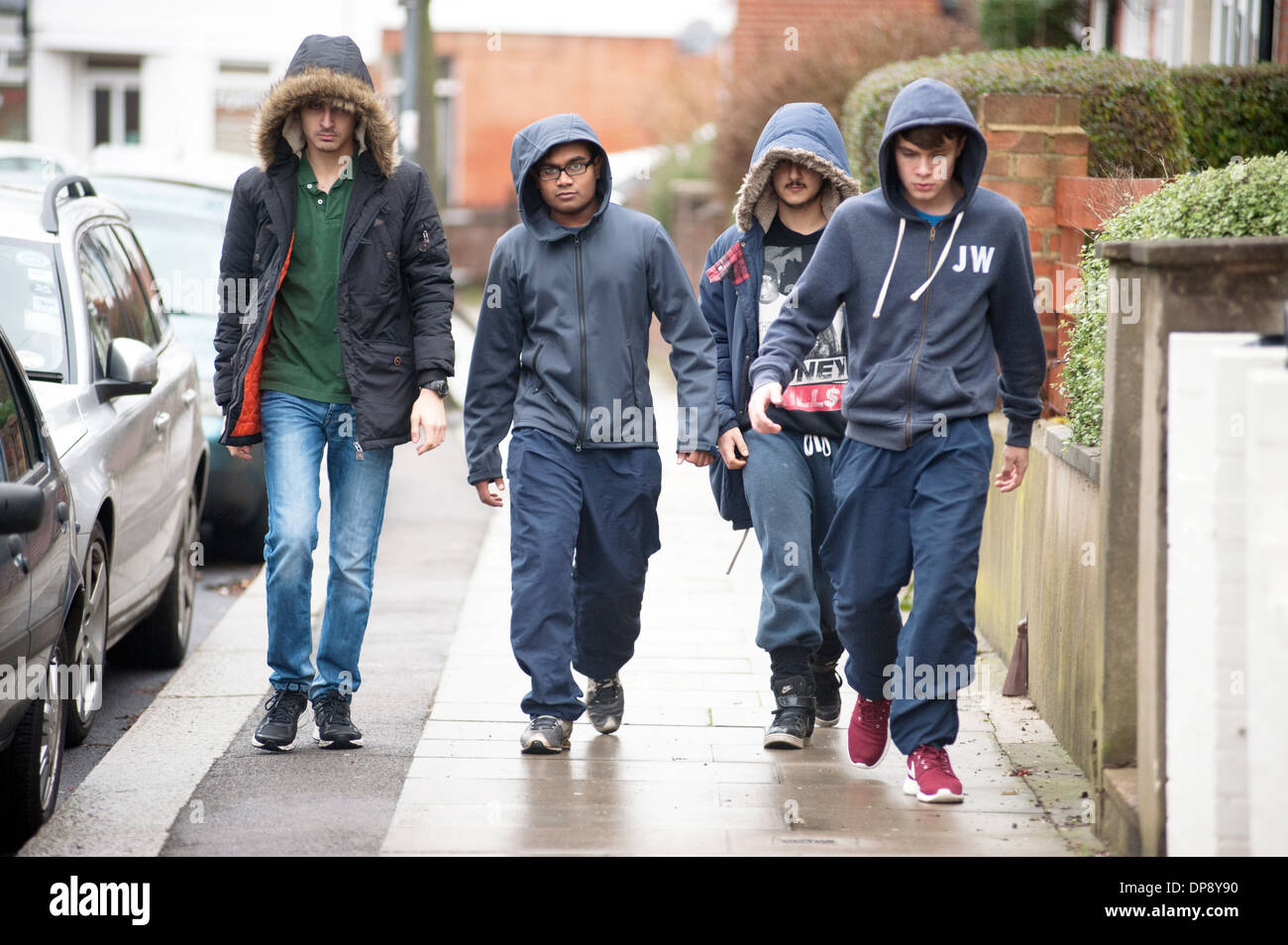 Un gruppo di ragazzi adolescenti in hoodies camminare insieme verso il basso una strada suburbana. Foto Stock