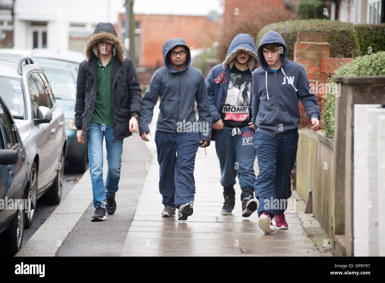 Un gruppo di ragazzi adolescenti in hoodies camminare insieme verso il basso una strada suburbana. Foto Stock