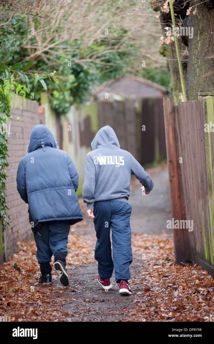 Due ragazzi adolescenti in hoodies camminare insieme verso il basso un vicoletto suburbana. Foto Stock