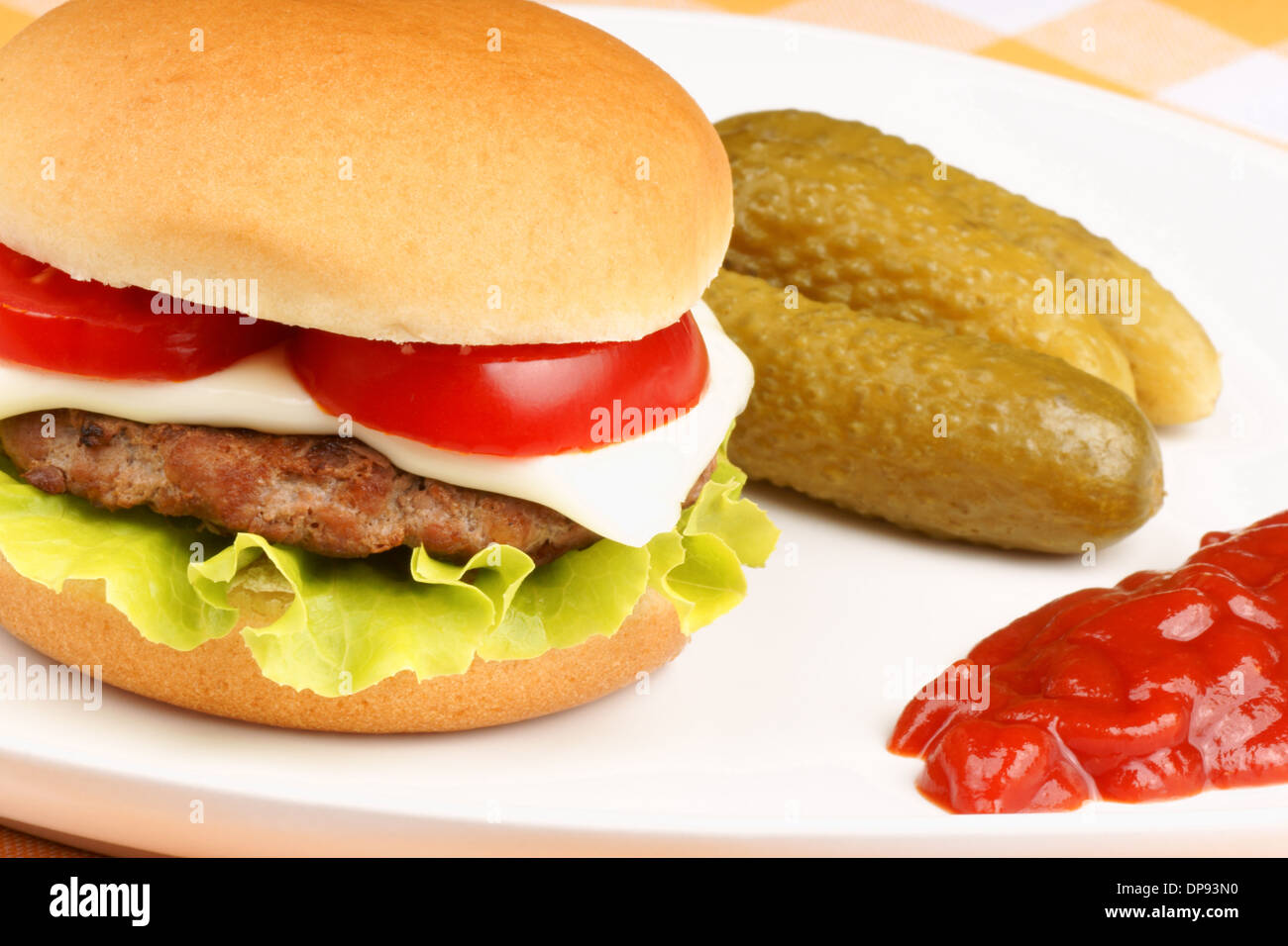 Primo piano di una mini formaggio hamburger con pomodoro e lattuga e alcuni sottaceti e ketchup su un piatto bianco. Foto Stock