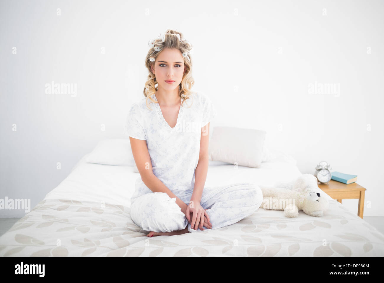 Una splendida bionda seduta sul letto confortevole Foto Stock