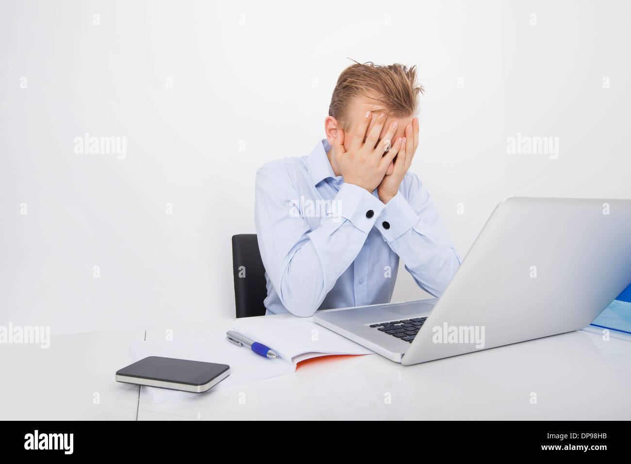 Stanco imprenditore con le mani sul viso seduto alla scrivania dal computer portatile Foto Stock