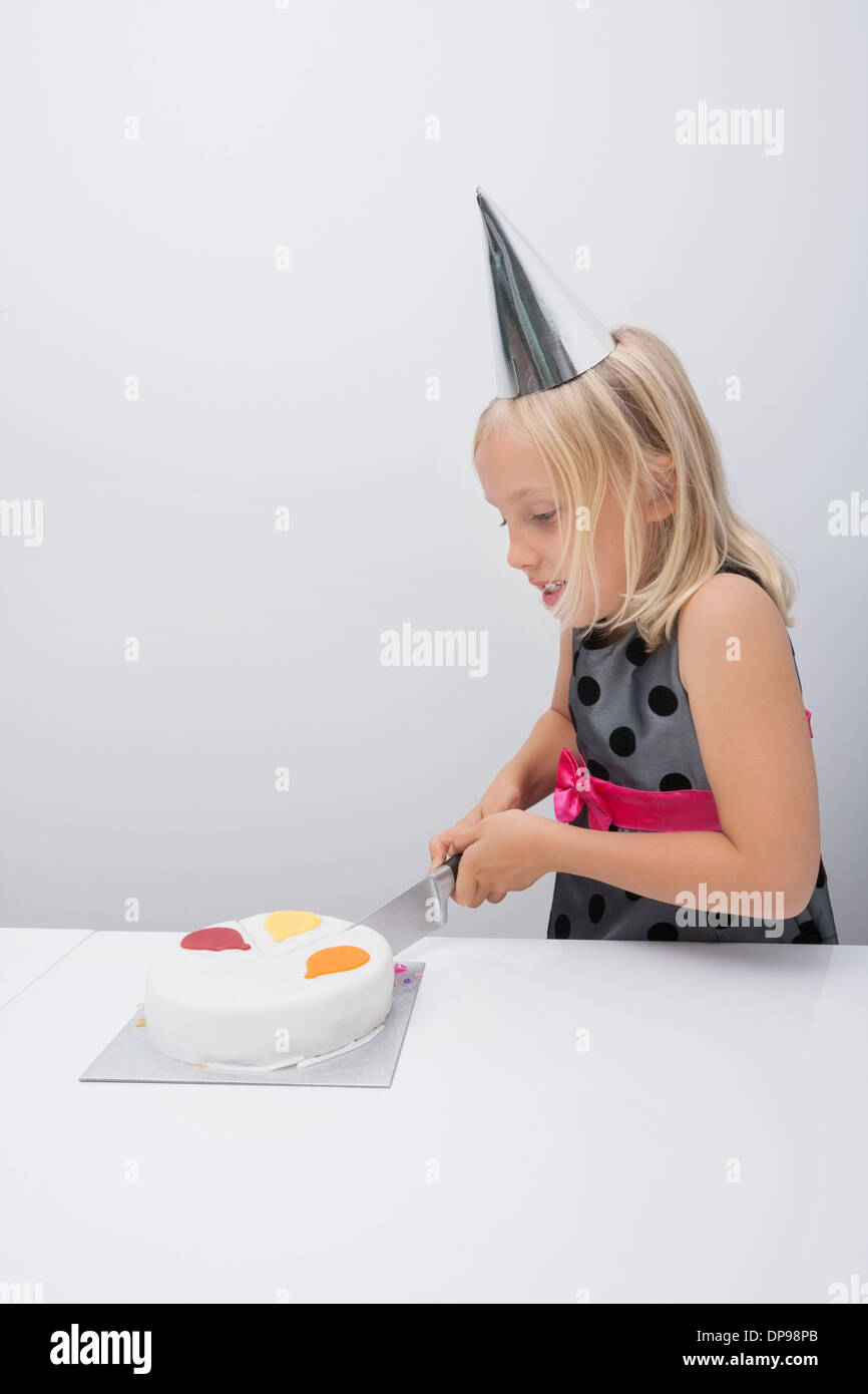 Ragazza carina il taglio di torta di compleanno a tavola in casa Foto Stock