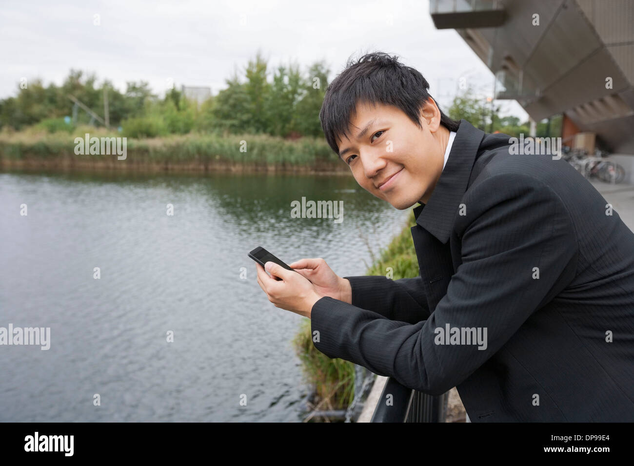 Ritratto di happy businessman con un telefono cellulare appoggiato sulla ringhiera del ponte Foto Stock