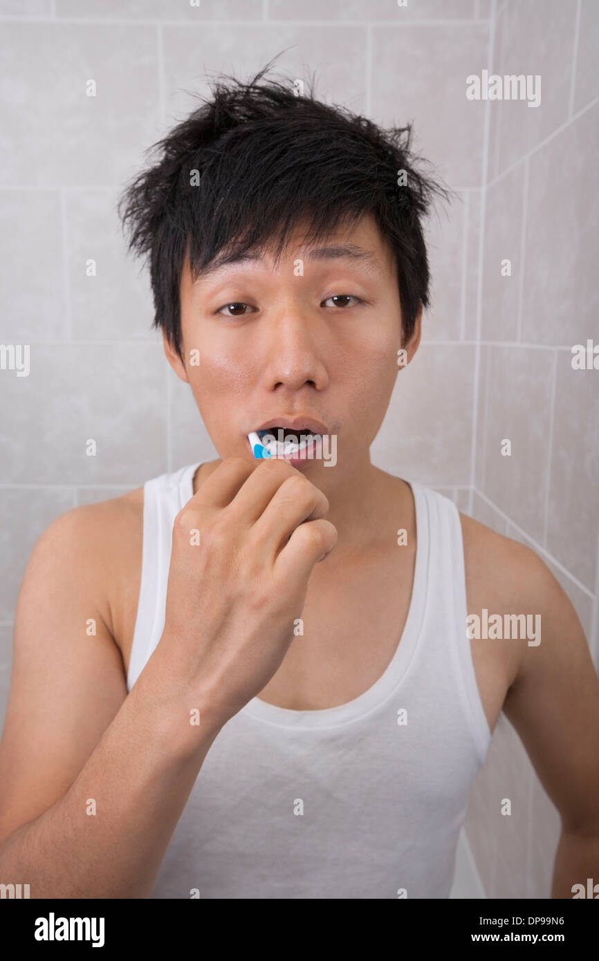 Assonnato metà uomo adulto spazzolare i denti in bagno Foto Stock