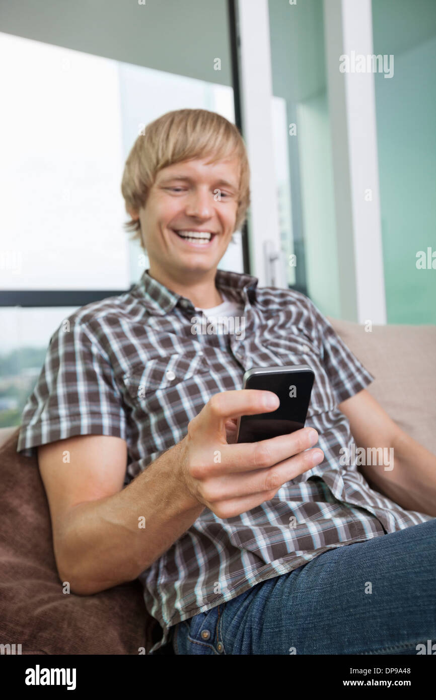 Allegro metà uomo adulto per la messaggistica di testo sul divano di casa Foto Stock