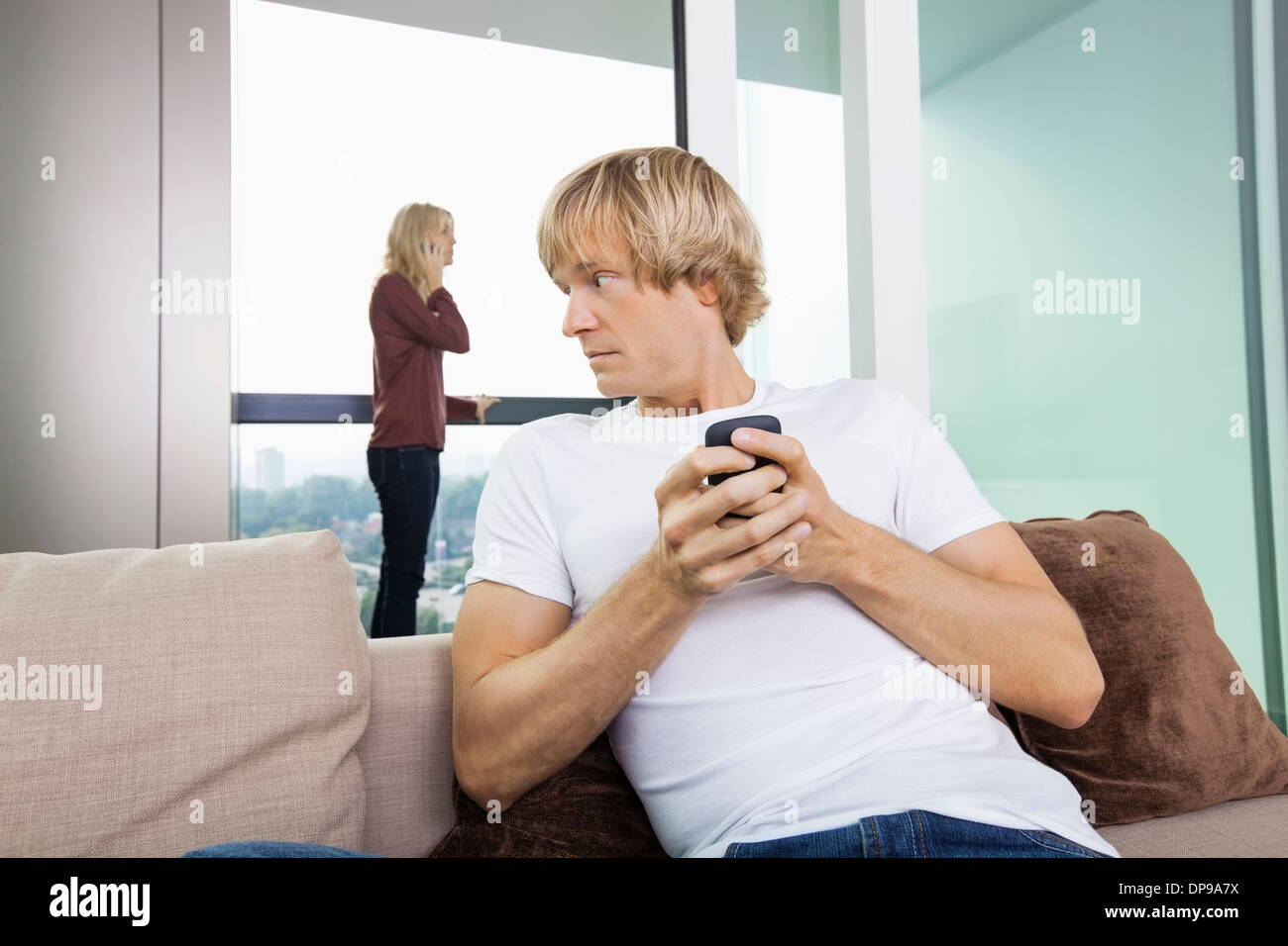 Metà di uomo adulto per la messaggistica di testo mentre donna utilizzando il cellulare in background a home Foto Stock