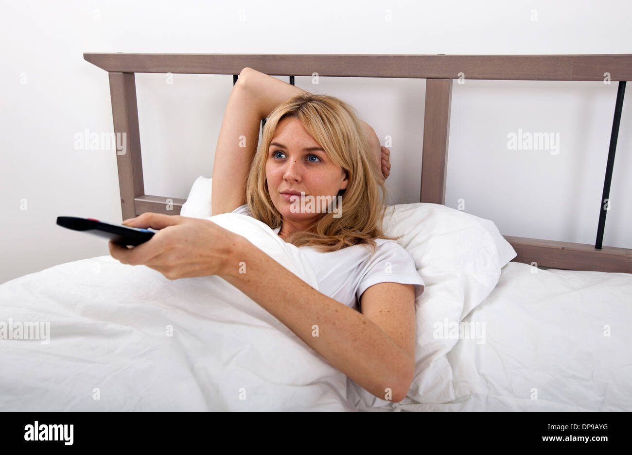 Giovane donna cambiando canali con telecomando a letto Foto Stock