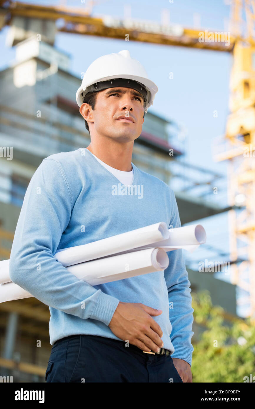 Architetto maschio con arrotolato blueprint permanente al sito in costruzione Foto Stock