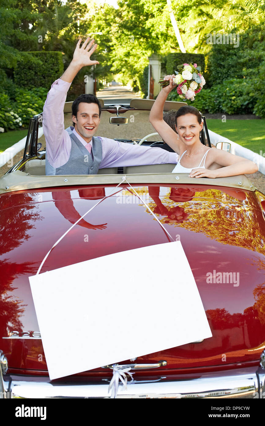 Happy sposi novelli sventolare nel convertibile con segno bianco in primo piano Foto Stock