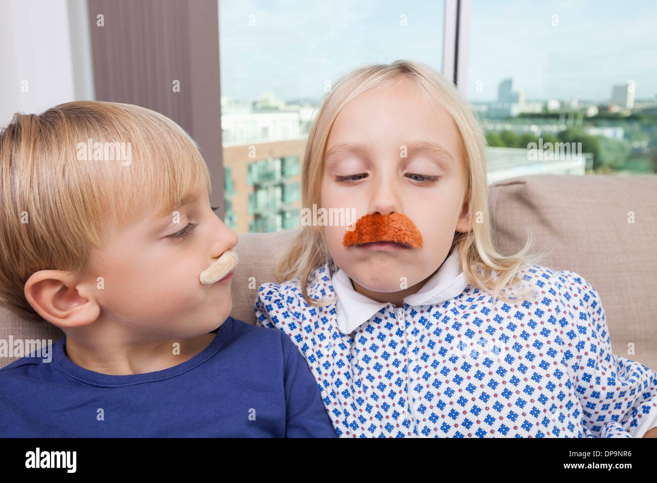 Fratello e Sorella indossa baffi artificiali a casa Foto Stock