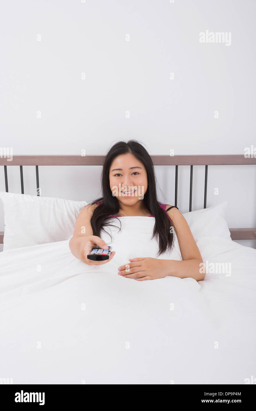 Ritratto di donna sorridente cambiando canali con telecomando a letto Foto Stock