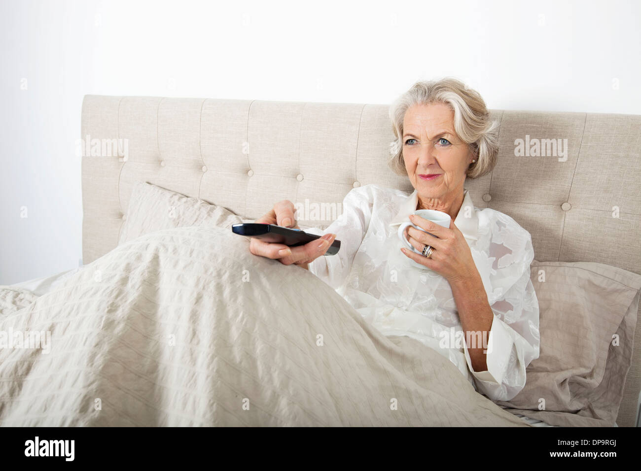 Senior donna guardare la TV mentre un caffè a letto Foto Stock