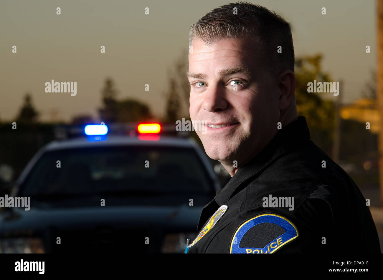 Un sorridente funzionario di polizia con la sua auto di pattuglia in background. Foto Stock