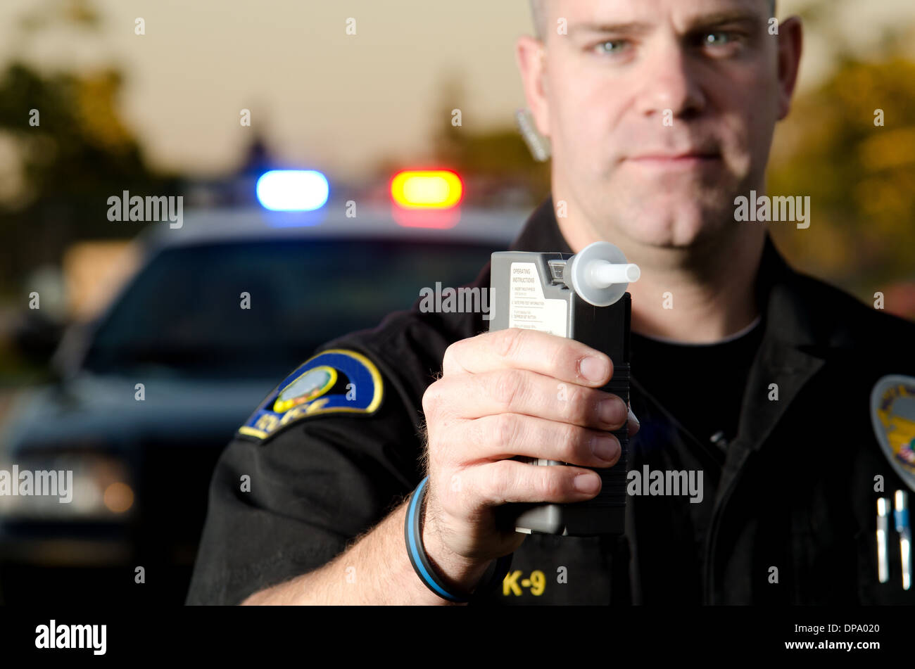 Un funzionario di polizia detiene un test del respiro macchina nella sua mano pronti a fermare il traffico con la sua auto di pattuglia in background. Foto Stock