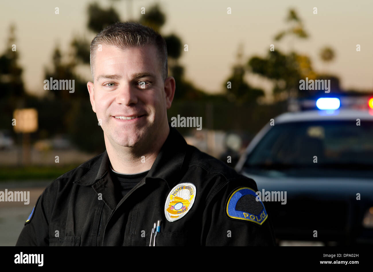 Un cortese e sorridente alla ricerca funzionario di polizia con la sua auto di pattuglia in background. Foto Stock
