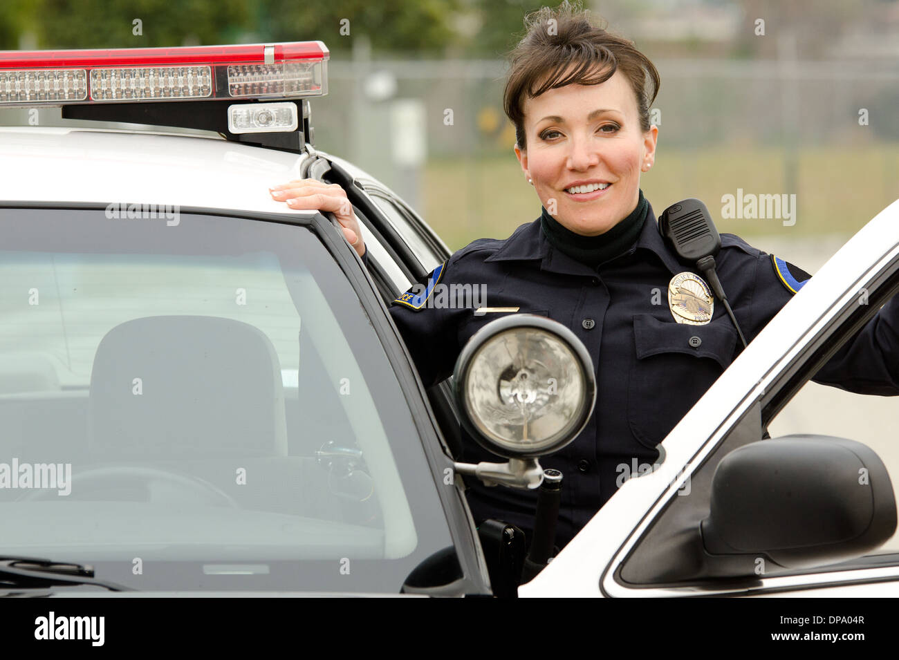 Un cordiale e sorridente femmina ispanica ufficiale con la sua auto di pattuglia. Foto Stock
