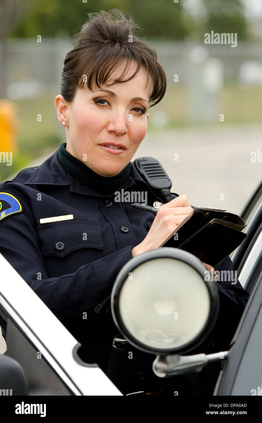 Una femmina di funzionario di polizia scrive un biglietto in piedi accanto alla sua auto di pattuglia. Foto Stock