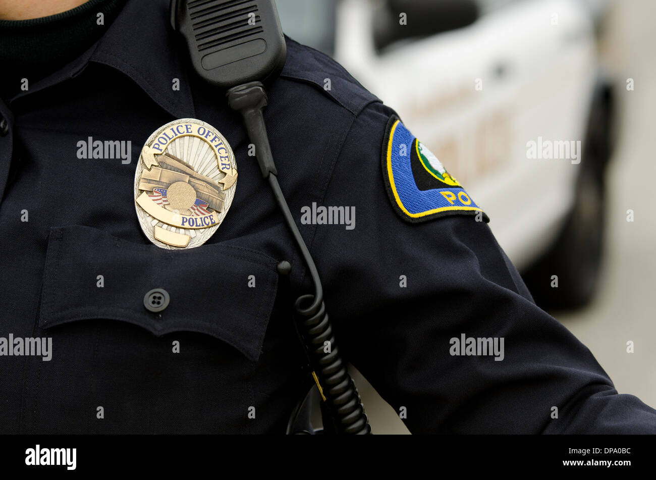 Una vista ravvicinata di un funzionario di polizia è uniforme e stemma con le auto della polizia in background. Foto Stock