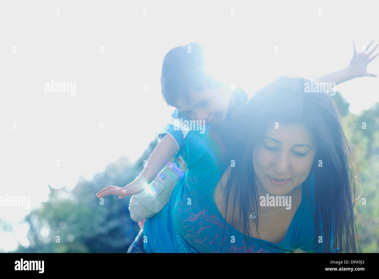 Ragazzo equitazione sulla madre la schiena con braccia tese Foto Stock