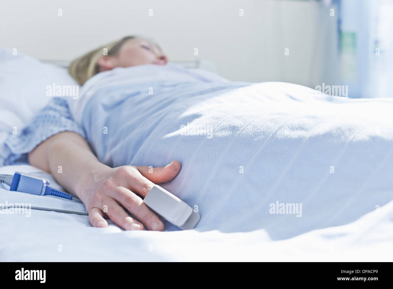 Paziente sdraiato sul letto di ospedale con monitor sul dito Foto Stock