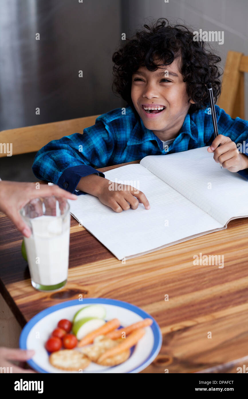 Ragazzo facendo i compiti, persona che serve spuntini e latte Foto Stock