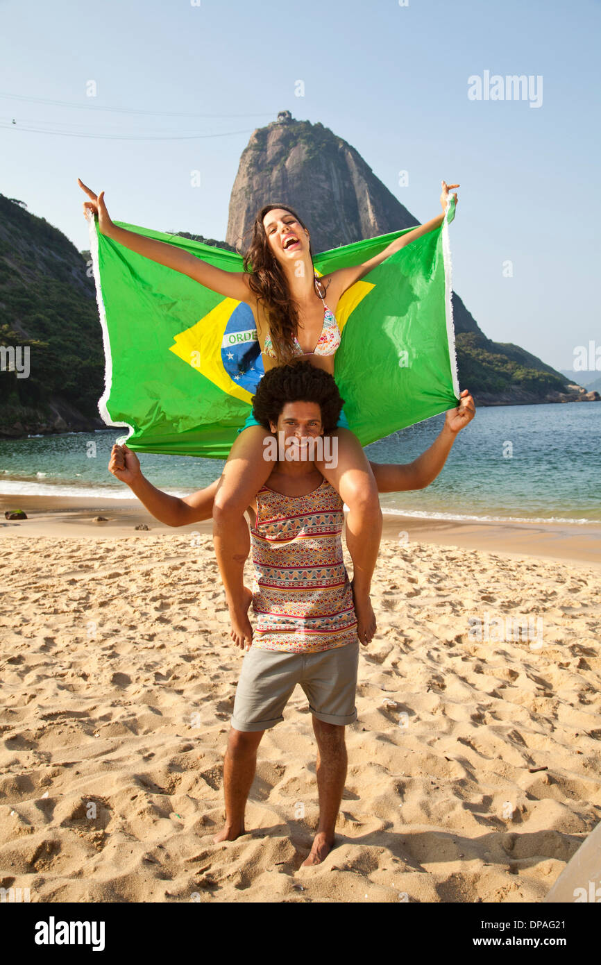 Coppia sulla spiaggia con bandiera brasiliana, Rio de Janeiro, Brasile Foto Stock