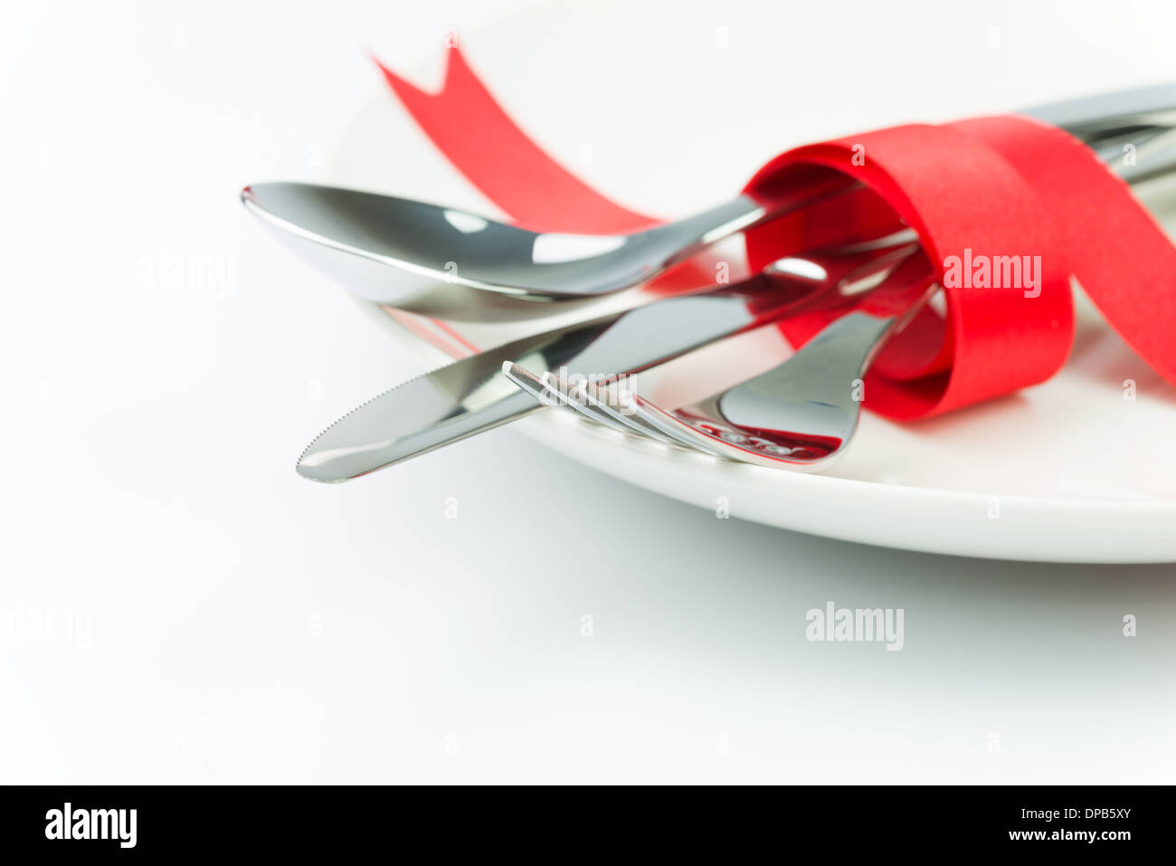 Forchetta, cucchiaio e il coltello legato con un nastro rosso su una piastra Foto Stock