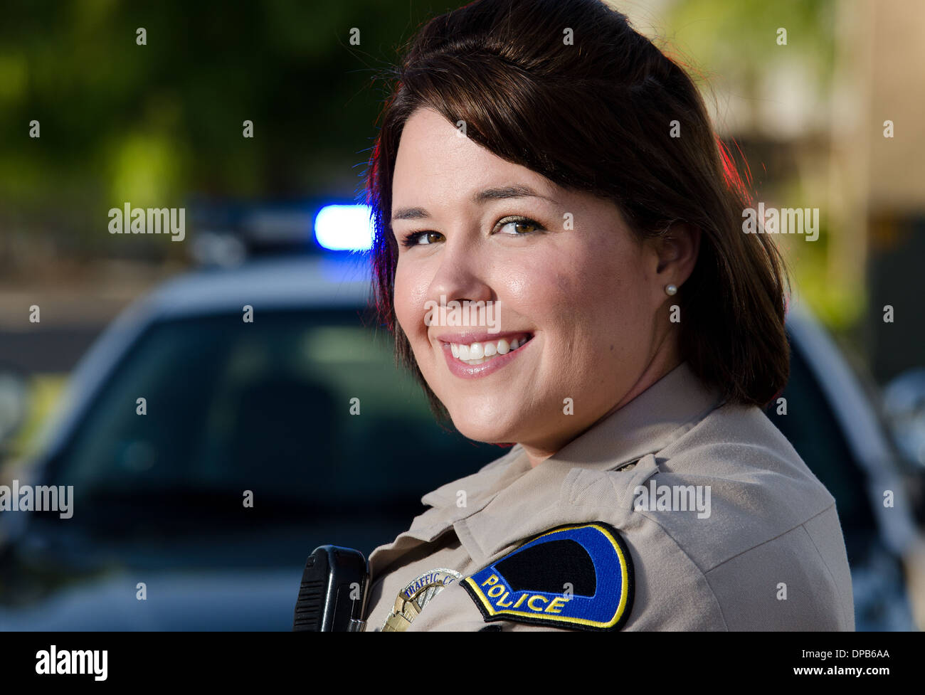 Una femmina di funzionario di polizia sorrisi come essa si erge di fronte alla sua auto di pattuglia. Foto Stock