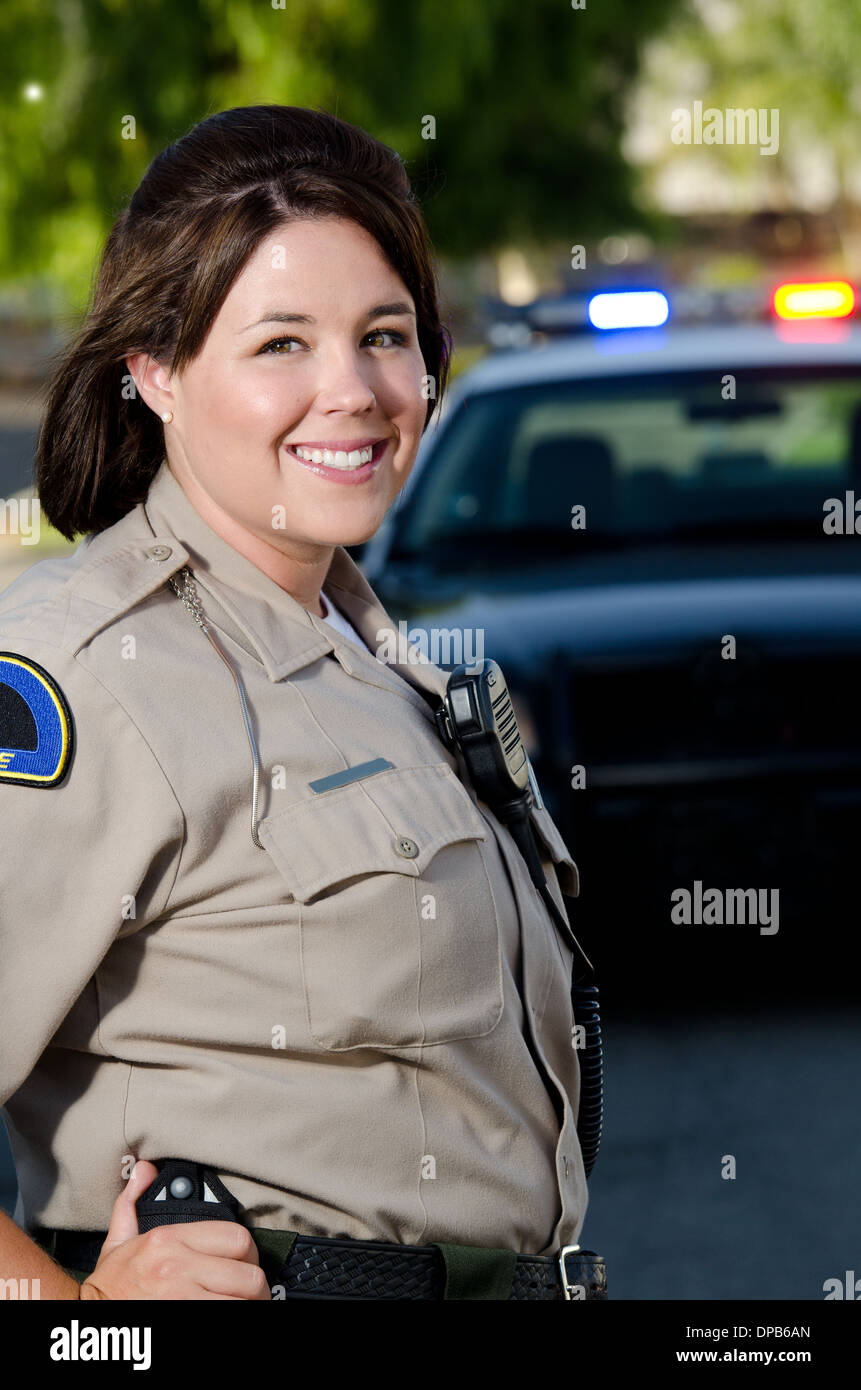 Una femmina di funzionario di polizia sorrisi come essa si erge di fronte alla sua auto di pattuglia. Foto Stock