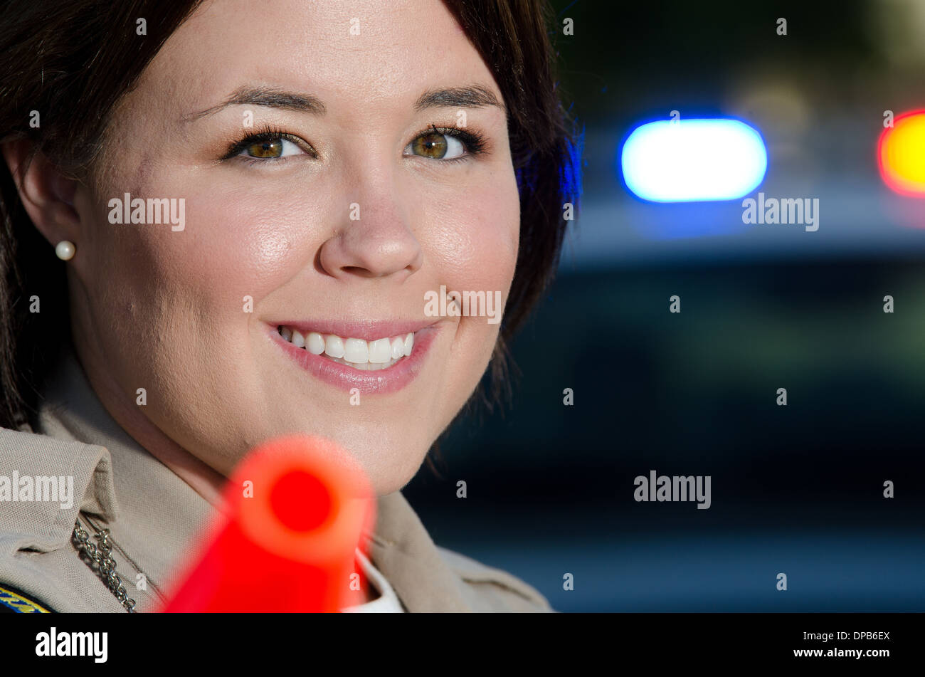 Un sorridente femmina offficer polizia mantiene la sua torcia elettrica con il suo cono arancione come sta circa per indirizzare il traffico. Foto Stock