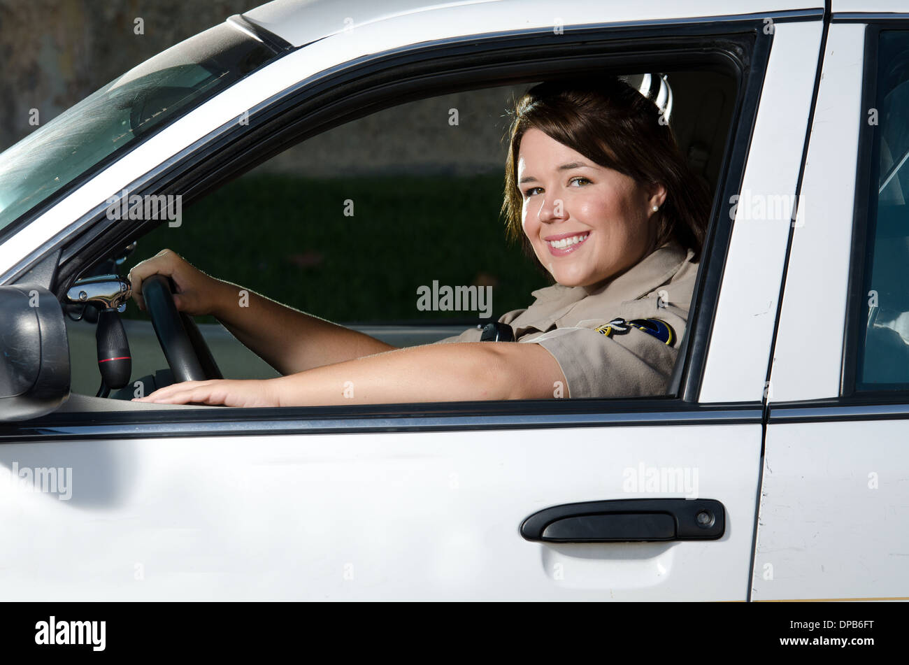 Un amichevole cercando donne funzionario di polizia si siede e sorrisi nella sua auto di pattuglia. Foto Stock
