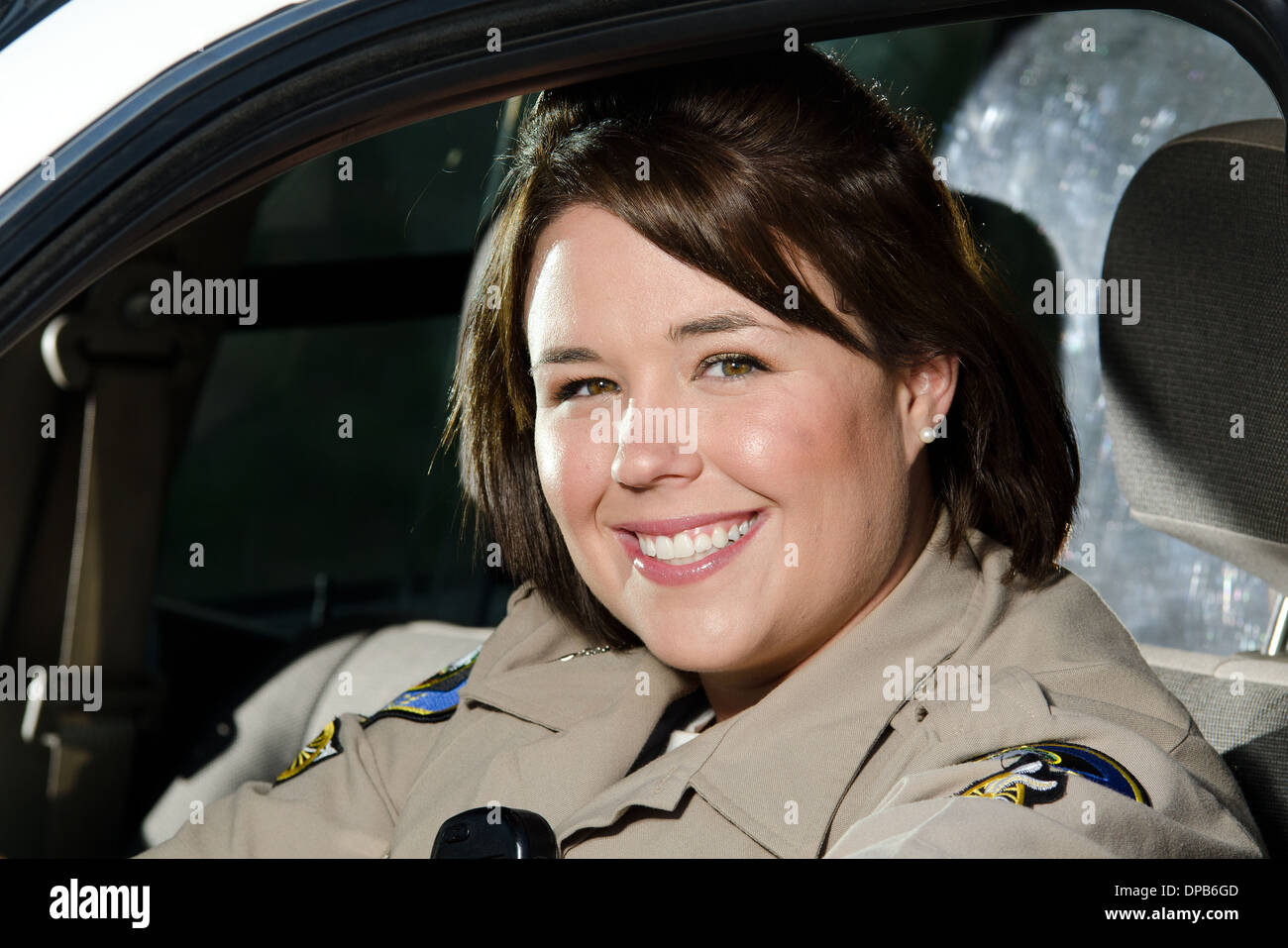 Un amichevole cercando donne funzionario di polizia si siede e sorrisi nella sua auto di pattuglia. Foto Stock