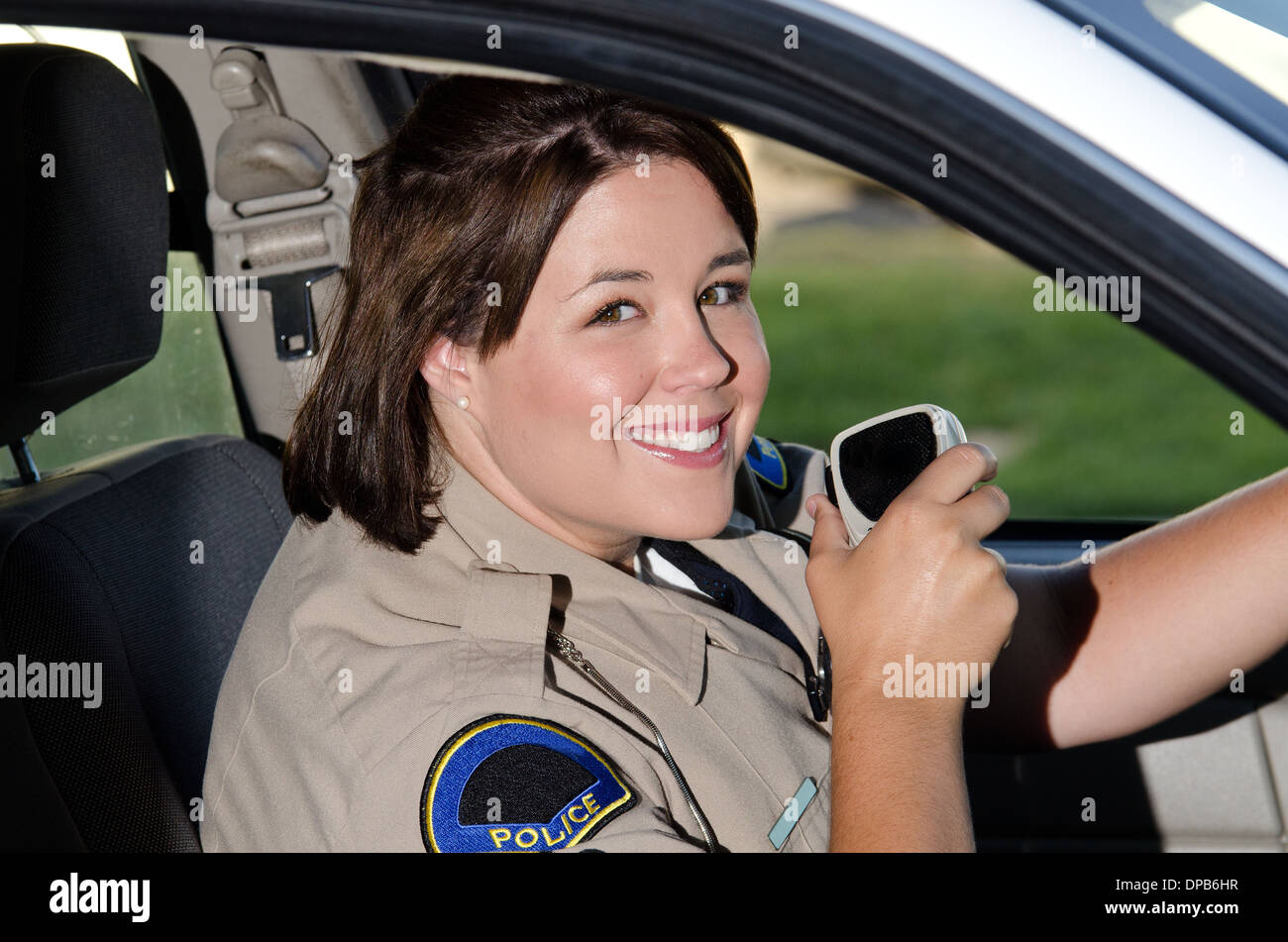 Una femmina di funzionario di polizia si siede nella sua auto di pattuglia come lei è in procinto di parlare alla radio. Foto Stock
