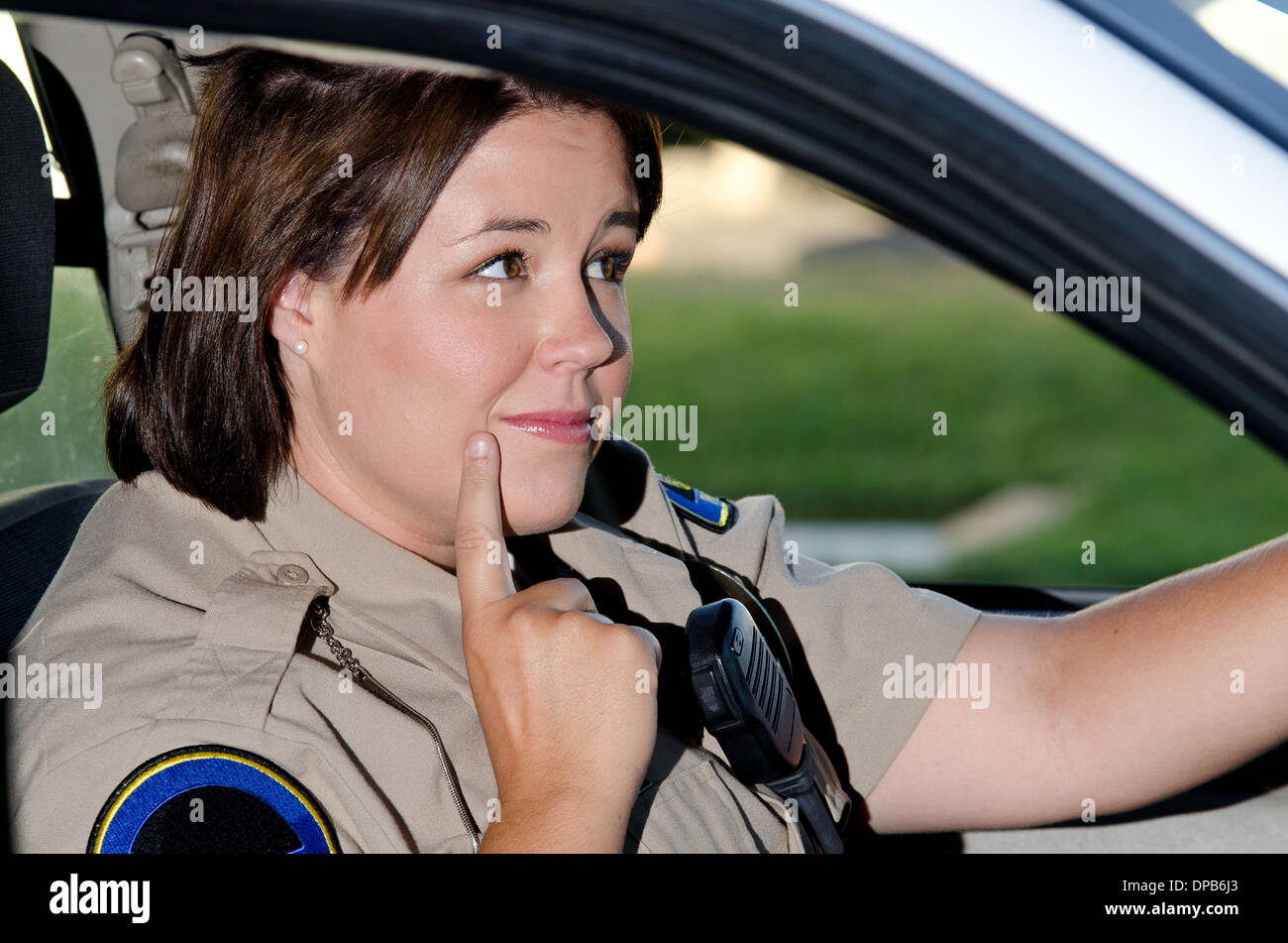 Una femmina di funzionario di polizia si siede nella sua auto di pattuglia come lei chiede cosa fare. Foto Stock