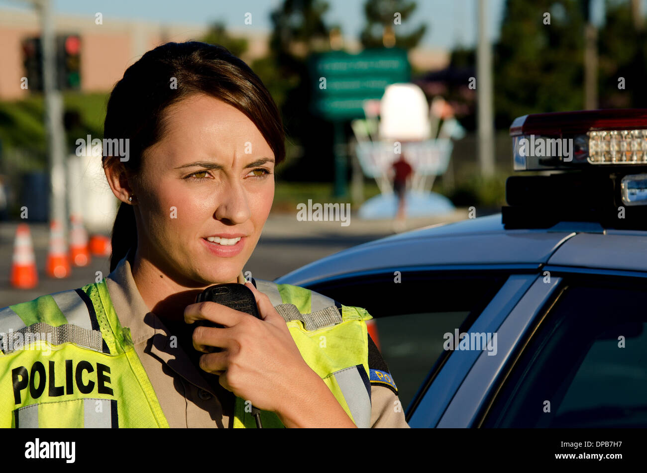 Una femmina di funzionario di polizia i colloqui sulla sua radio mentre in piedi accanto alla sua auto di pattuglia. Foto Stock