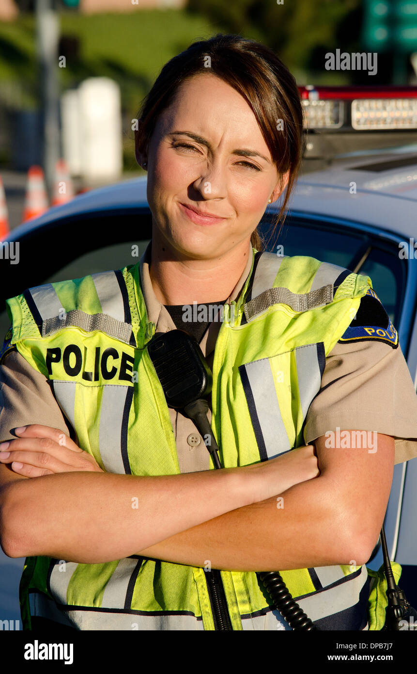 Una femmina di funzionario di polizia con un cipiglio sul suo viso come lei incrocia le braccia davanti a lei partrol auto. Foto Stock