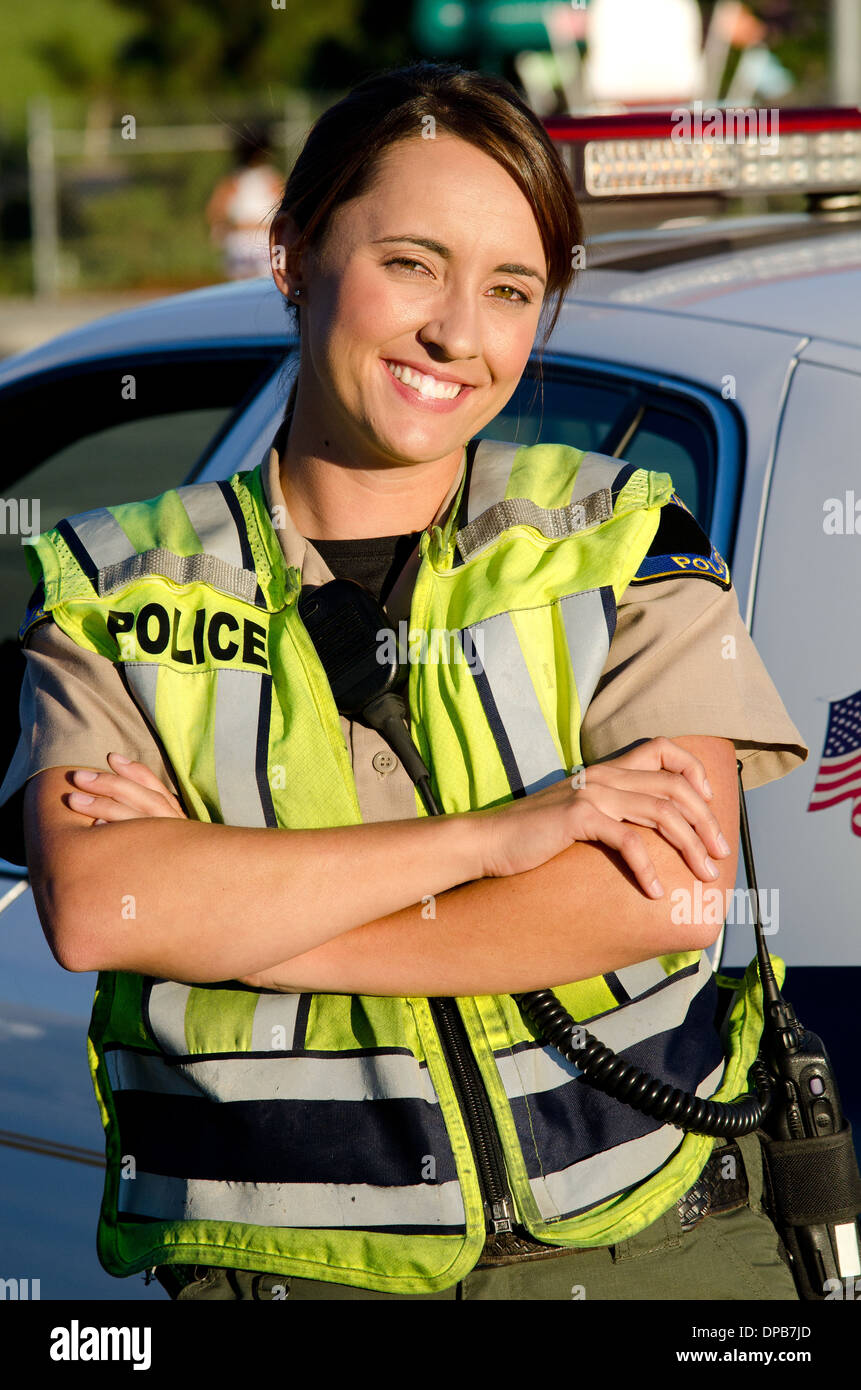 Una femmina di funzionario di polizia di sorridere quando lei incrocia le braccia davanti a lei partrol auto. Foto Stock