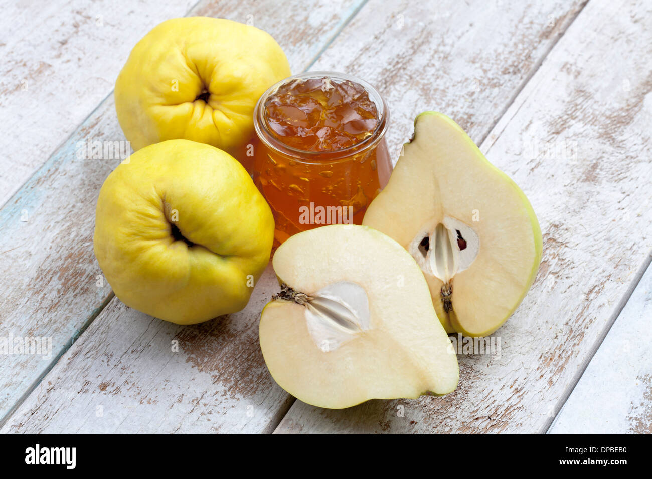 Due e una metà cotogne (Cydonia oblonga) e un bicchiere di marmellata di mele cotogne sul pannello di legno Foto Stock