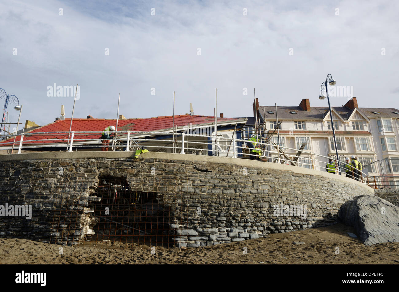 Aberystwyth, Wales, Regno Unito. Il 10 gennaio 2014. Una settimana dopo una violenta tempesta a sovracorrenti e gale force venti danneggiato Aberystwyth sul lungomare, detriti è ancora sparsi intorno alla zona. I lavoratori del consiglio di grado i depositi di alluvione con macchine per separare la sabbia e la pavimentazione in lastre. Lavoro inizia lo smantellamento del grado 2 elencati rifugio pubblico, il Minato le fondazioni di cui ha precedentemente conteneva un capanno in stile vittoriano e, ripetutamente, il sito della città patibolo. Credito: keith burdett/Alamy Live News Foto Stock