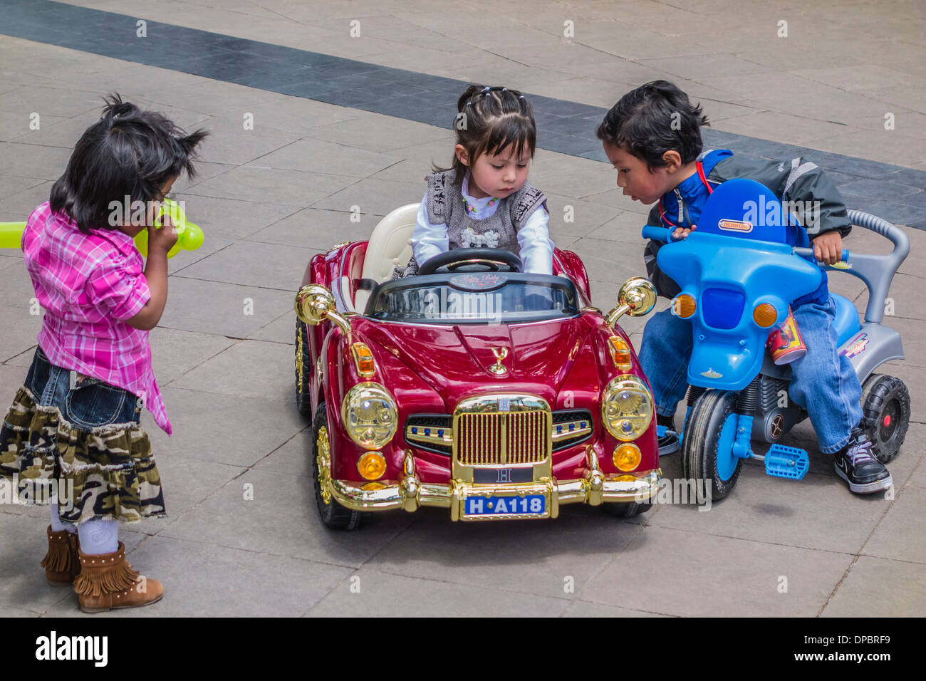 Una classe superiore ragazza boliviana si siede nella sua molto fancy giocattolo auto mentre due poveri bambini indigeni stanno a guardare in Plaza 25 de Mayo, Sucre. Foto Stock