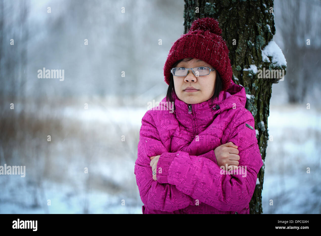 Giovani e moody ragazza asiatica con una camicia rosa appoggiata contro un albero in inverno Foto Stock