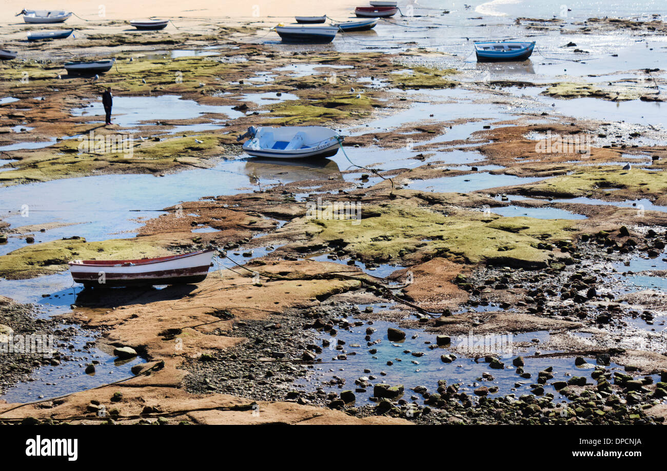 Cadiz, Spagna. Figura solitaria fra le piccole barche di pescatori sulla spiaggia con la bassa marea. Foto Stock