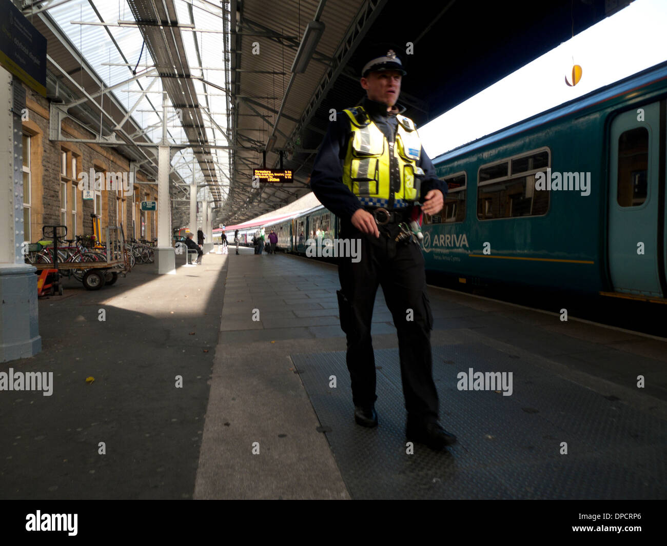 Poliziotto dei trasporti britannico uomo della polizia che cammina lungo la piattaforma ferroviaria presso una stazione ferroviaria di Cardiff Galles Gran Bretagna Regno Unito KATHY DEWITT Foto Stock